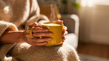 A person holding a warm, golden turmeric latte for comfort while feeling run-down with a seasonal cold