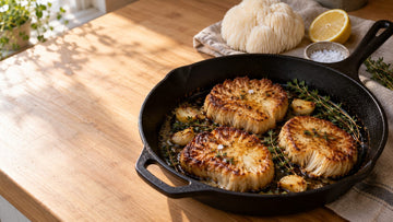 Golden pan-seared lion's mane mushroom steaks with garlic and thyme in a cast iron skillet next to a fresh white lion's mane mushroom