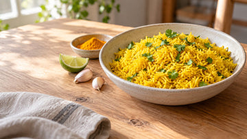 A bowl of fluffy yellow turmeric rice topped with chopped cilantro, with a lime wedge and a small dish of ground turmeric beside it